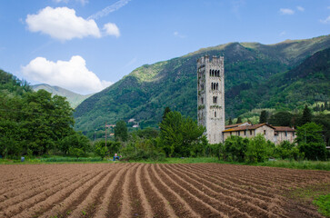 Il campanile di una chiesa e un campo arato nella campagna della valle del Serchio lungo la Via del Volto Santo, cammino che parte da Pontremoli e arriva a Lucca