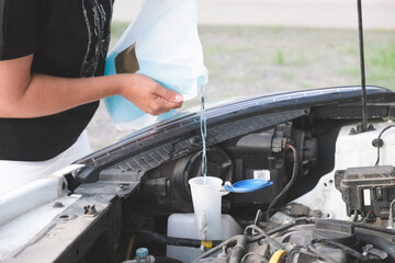 Woman pours windshield cleaning fluid. Flow windshield fluid into the windshield washer reservoir....