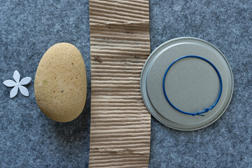 paper flower, rounded stone (worn brick), corrugated cardboard, metal disc, and loop earring on gray felt
