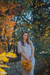 Portrait of beautiful woman in white dress holding bouquet with autumn leaves.