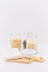 barattoli in vetro con riso integrale da agricoltura biologica, scodella, tagliere in legno e canovaccio su tavolo bianco