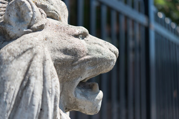 stone garden lion made from cast concrete near a fence in the city