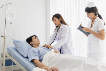 Female doctor and nurse visiting and using stethoscope checking examine heartbeat male patient at hospital
