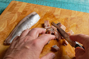 Man hands cutting pickled herring fillets into pieces, on wooden cutting board.