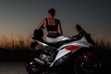 Fototapeta na wymiar young biker woman with short hair watching the sunset leaning on her motorcycle after a road trip