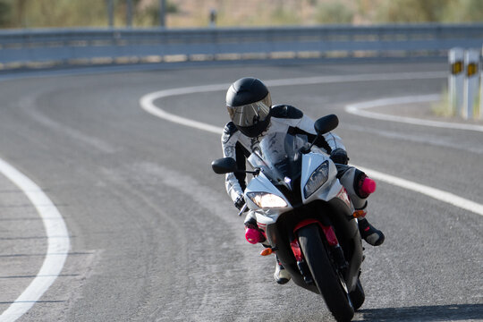 motorcyclist with suit and protective helmet taking a curve on a paved road