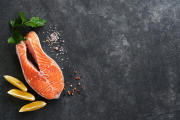 Salmon. Raw salmon steak. Fresh raw salmon fish with cooking ingredients, herbs and lemon prepared for grilled baking on black background. Healthy food. Top view. Copy space.