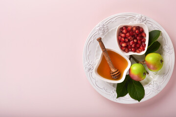 Rosh Hashanah. Honey jar, honeycomb, apple and pomegranate on simple pink background. Jewish New Year holiday greeting card. Rosh Hashanah holiday attributes. Space for text