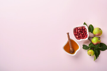 Rosh Hashanah. Honey jar, honeycomb, apple and pomegranate on simple pink background. Jewish New Year holiday greeting card. Rosh Hashanah holiday attributes. Space for text