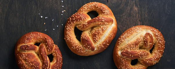 Naklejka premium Bavarian pretzels and glass of lager beer. Oktoberfest food menu, traditional salted pretzels over old dark wooden background. Top view with space for text. Oktoberfest theme