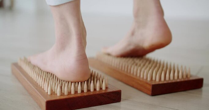 A piece of sadhu wooden board with nails, female feet stepping on sharp nails for meditation, foot relaxation, acupuncture tool. sadhu board with sharp nails, relaxation exercise, yoga.
