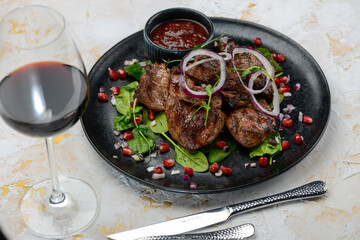 fried shish kebab in a black plate with salad and pomegranate berries on a white background with a glass of wine
