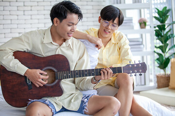 Asain gay couple playing guitar together in home, LGBTQ concept.