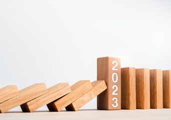 Close-up the 2023 year numbers calendar on wooden cube blocks stops falling blocks and collapsing dominoes on table on white background. Preventing the domino effect and staying strong concept banner.