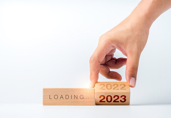 Loading to 2023 happy new year. Hand flipping the 2022 to 2023 year numbers calendar on wooden cube blocks isolated on white background to prepare for new year change and start new business target.