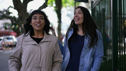 Female friends laughing and smiling while while walking in city sidewalk. Authentic real expression laugh and smile