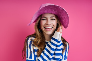 Attractive young woman in pink hat smiling while standing against colored background