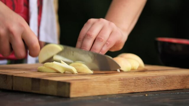 Woman's hands cut apples into pieces on a wooden cutboard, natural colors and black background. Woman cut apples with the use of professional knife.