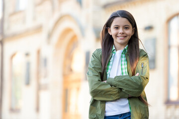 Happy teen girl model keeping arms crossed in casual trendy fashion style outdoors, copy space