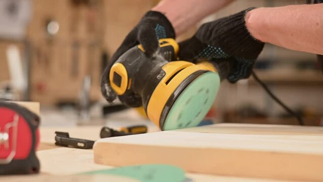 Man using orbital wood sander in workshop. 