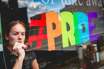 Girl decorating a shop window with a Gay Pride sign supprting diversity