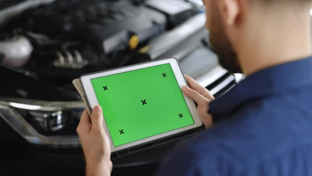 Car Service Manager or Mechanic Uses Tablet Computer with Green Screen Mock Up that is Pointed at an Enginer Bay. Specialist Inspecting the Vehicle in Order to Find Broken Components In the Engine