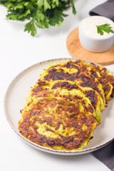 Vegetarian zucchini fritters or courgettes pancakes, served with fresh herbs and sour cream.