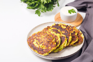 Vegetarian zucchini fritters or courgettes pancakes, served with fresh herbs and sour cream.