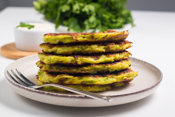 Vegetarian zucchini fritters or courgettes pancakes, served with fresh herbs and sour cream.