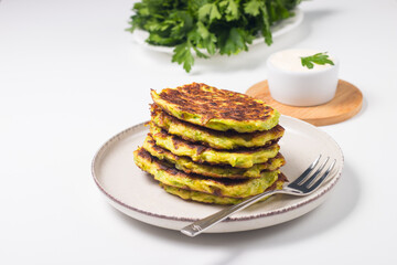 Vegetarian zucchini fritters or courgettes pancakes, served with fresh herbs and sour cream.