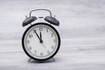 black vintage alarm clock standing on the table with color background shows 11hours 55 minutes in...