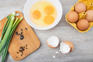 three eggs broken, green onions, eggs in a package, black peppercorns for cooking. Ingredient in the kitchen. Close up view of ingredients on breakfast.