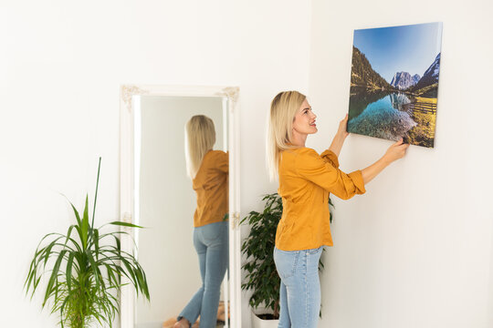 Canvas print with gallery wrap. Woman hangs photography on white wall. Hands holding photo canvas print