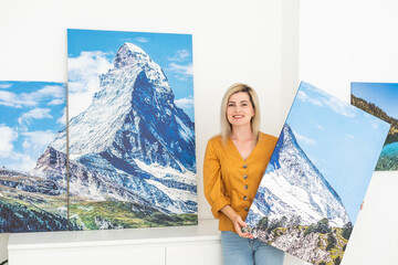 Canvas print with gallery wrap interior decor. Woman hangs landscape photography on white wall....