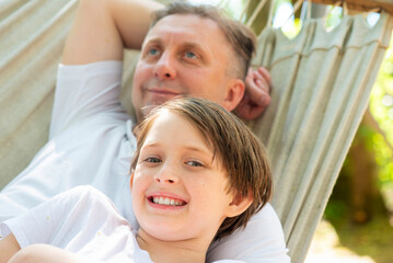 father and son rest lying on a hammock. son looks like his daddy. family vacation dad with a child.
