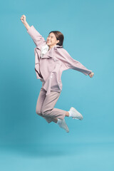 Young beautiful asian woman with smart casual cloth wearing pink coat jumping with excite feeling isolated on blue background