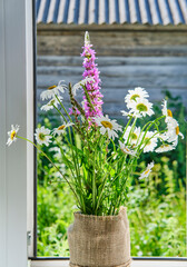 Bouquet of wild meadow flowers on window sill of rural house in sunlight. Close-up