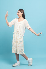 Beautiful young asian woman in white dress with flower pattern using smartphone isolated on blue background