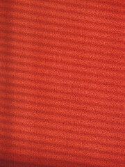 Red textured wall with blinds shadows, warm colors, vertical photo. Decorative background for design, ornament from parallel lines, backdrop or wallpaper