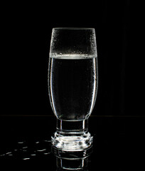 Glass of water on blue background with reflection in the mirror and water splashes