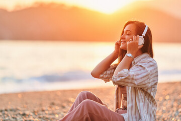 Calm serene alone woman with closed eyes enjoys of listening relax traveling music on the seashore at sunset time. Happy beautiful moment life