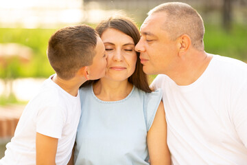Fototapeta premium Husband and son kiss a young beautiful woman on the cheeks