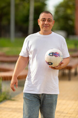 A young man in a white T-shirt walks with a ball in his hand