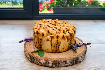 Homemade round bread with garlic butter and herbs, lying on a wooden board with basil leaves.