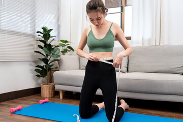 Sporty woman in sportswear is measuring waist circumference and looking on tape measure to checking