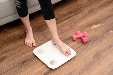 Sporty woman is stepping to weigh on electronic the scales to check results after diet and losing