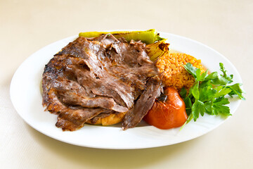 Turkish and Arabic Traditional Ramadan doner kebab with tasty tomato sauce and rice or turkish pilav in white plate on wood table background. ( Pilav ustu doner)
