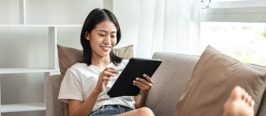 Obraz na płótnie Canvas Half-Japanese woman sitting on the sofa using tablet while on vacation, Rest at home, Living room, Relax time, Touch screen tablet, Go on internet, Favorite corner, Personal space