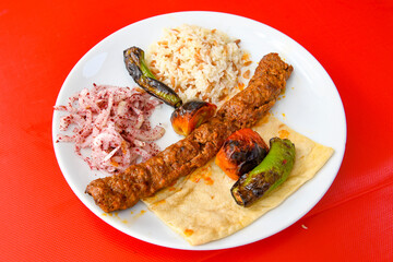 Grilled Turkish Adana, Urfa  Kebab with grilled vegetables, onion and rice on plate. Adana durum.
