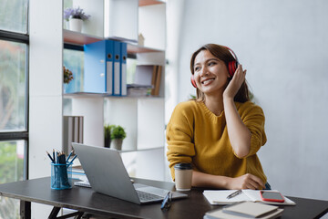 Happy woman is listening music via headset while working or study on laptop at home or office space.